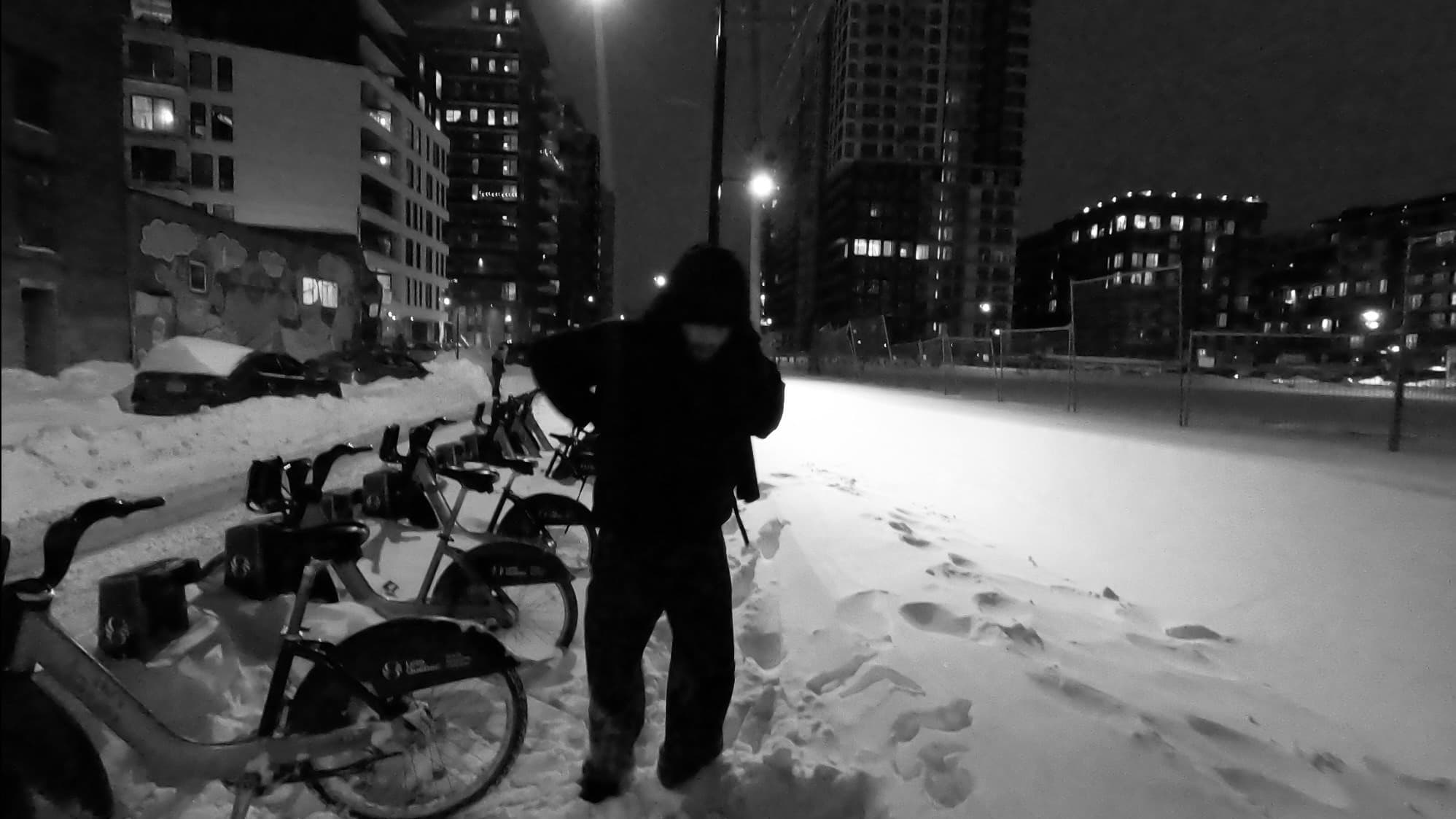 Person standing beside a row of bikes on a snowy city street at night